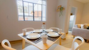 A dining area with a table set for four, white chairs, and a window with a view of buildings outside. - Capitalia | Chill Stay & Near Condesa & Museums (Ciudad de México)