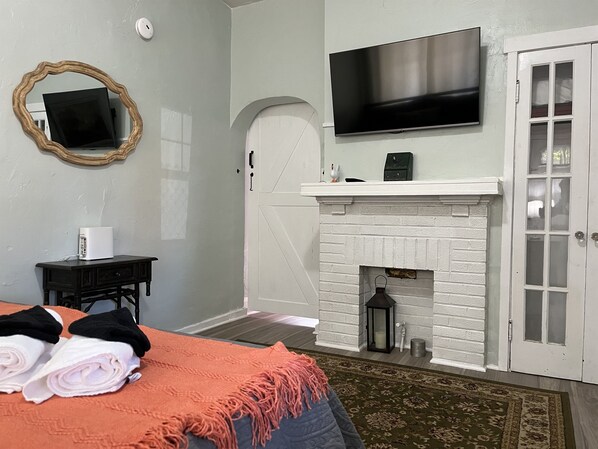 A bedroom with a bed, a TV mounted above a fireplace, a mirror on the wall, and a door with glass panels.