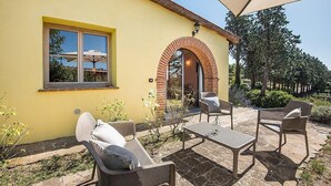 An outdoor patio with wicker furniture, a yellow building, and a large umbrella providing shade. - Casa Dracena Q: A welcoming cottage situated in the heart of the Tuscan countryside, with Free WI-FI. (Trequanda)