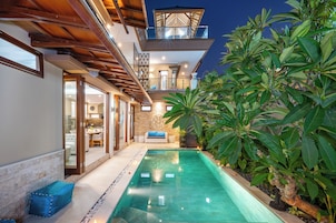 A modern house with a swimming pool, a balcony, and lush greenery.