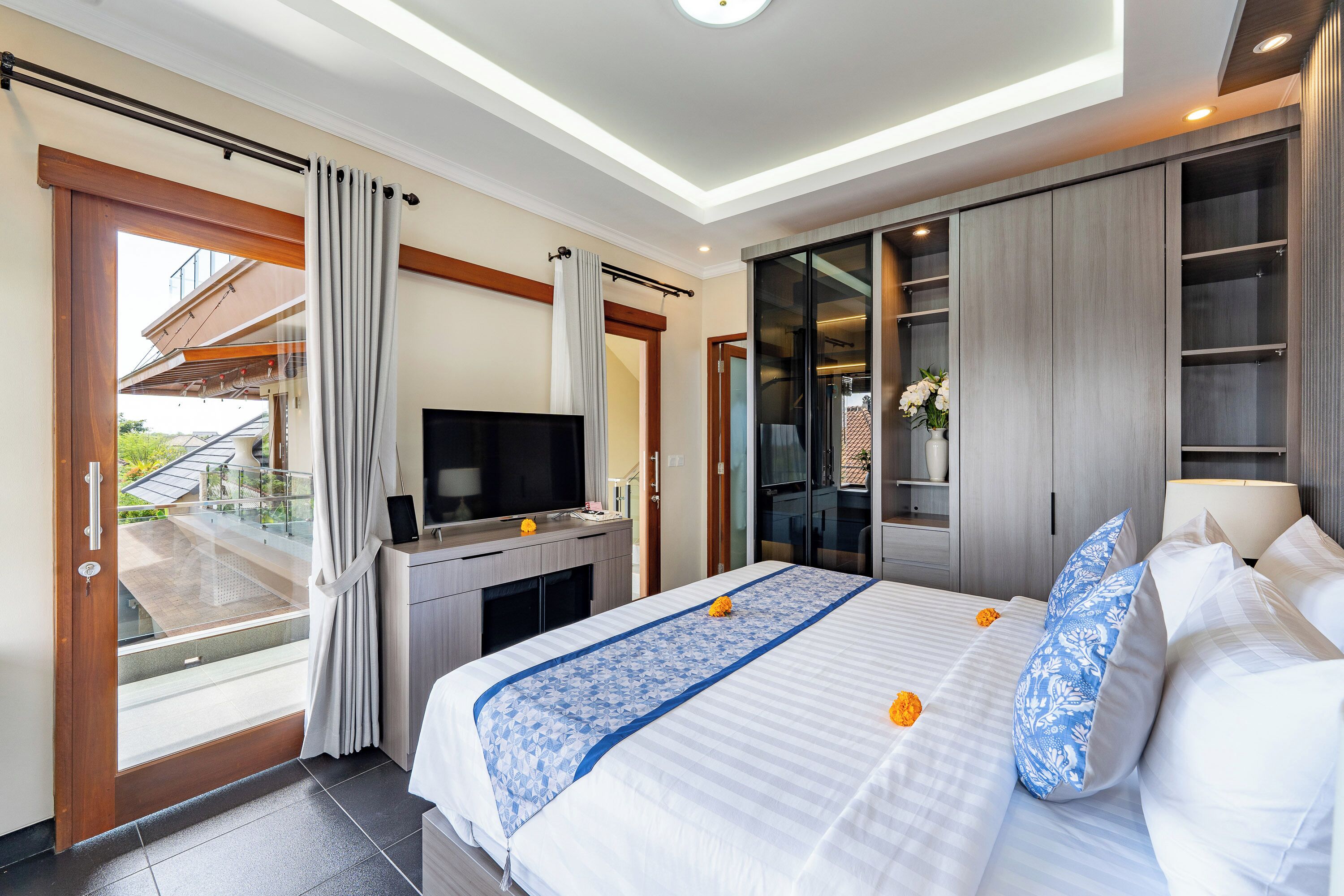 A modern hotel room with a large bed, a TV, a desk, and a sliding glass door leading to an outdoor area.