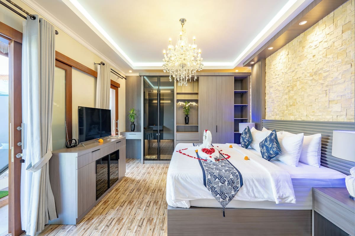 Ein modernes Hotelzimmer mit einem großen Bett, einem Fernseher, einer Kristallleuchtre und einer Wand aus Stein.