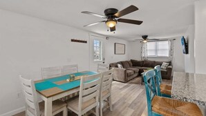 Ein kompakter Wohnbereich mit Essbereich, einer Couch, einem Deckenventilator und einem an der Wand befestigten Fernseher.