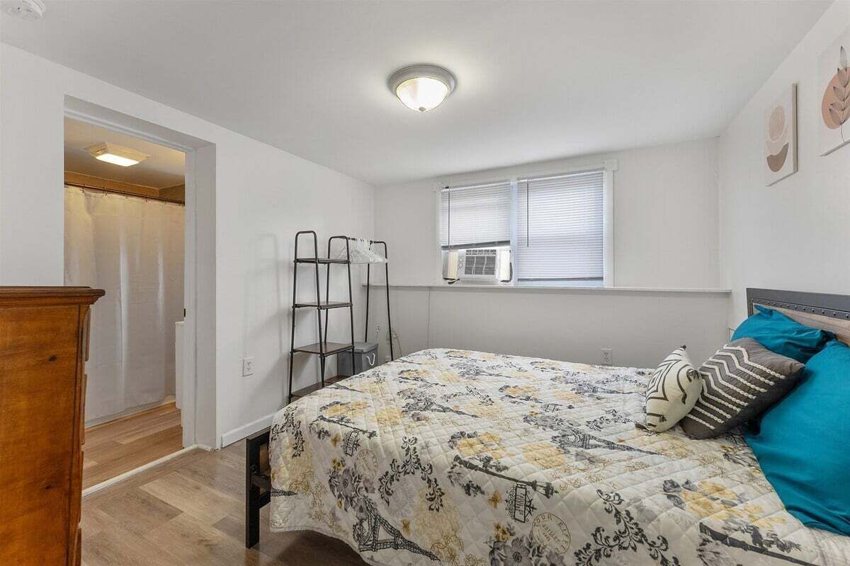 Un dormitorio con una cama, un ventanal con persianas, un radiador y una puerta que da a otra habitación.
