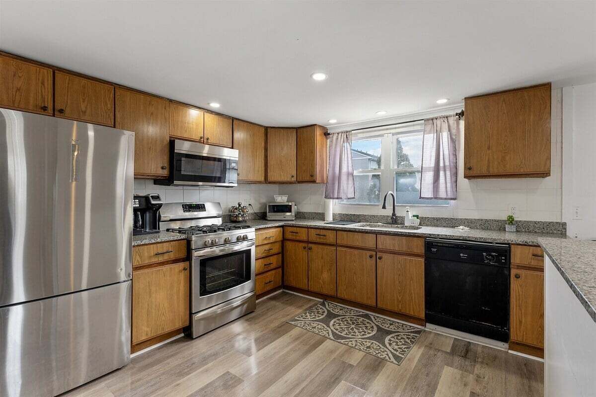 A modern kitchen with wooden cabinets, stainless steel appliances, and a patterned rug.
