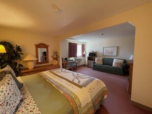 A hotel room with a bed, a desk, a chair, a sofa, and a television.