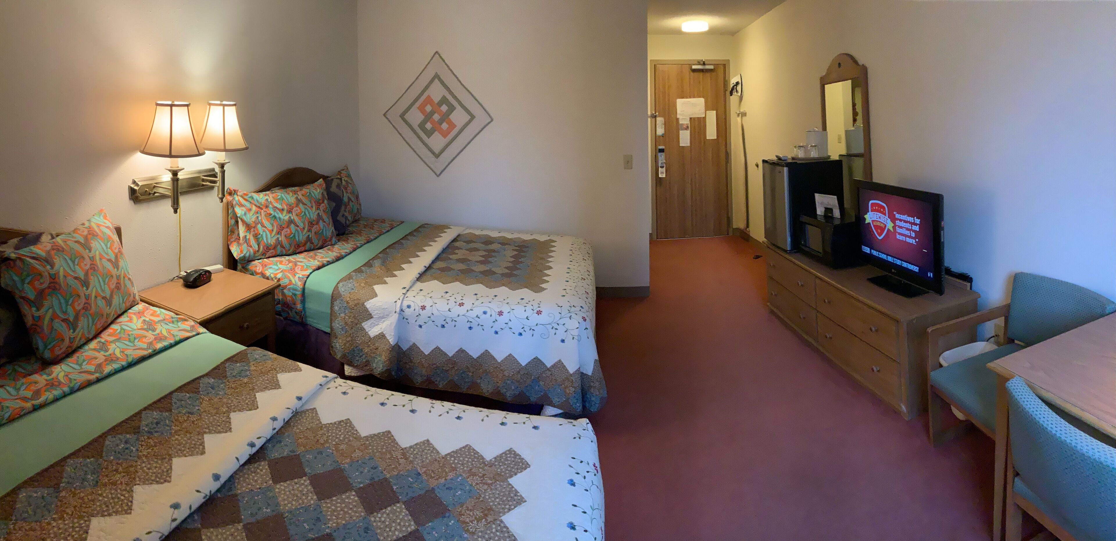A hotel room with two beds, a TV, a desk, and a dresser.