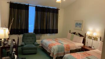 A hotel room with two beds, a desk, a chair, a ceiling fan, and a window with curtains.