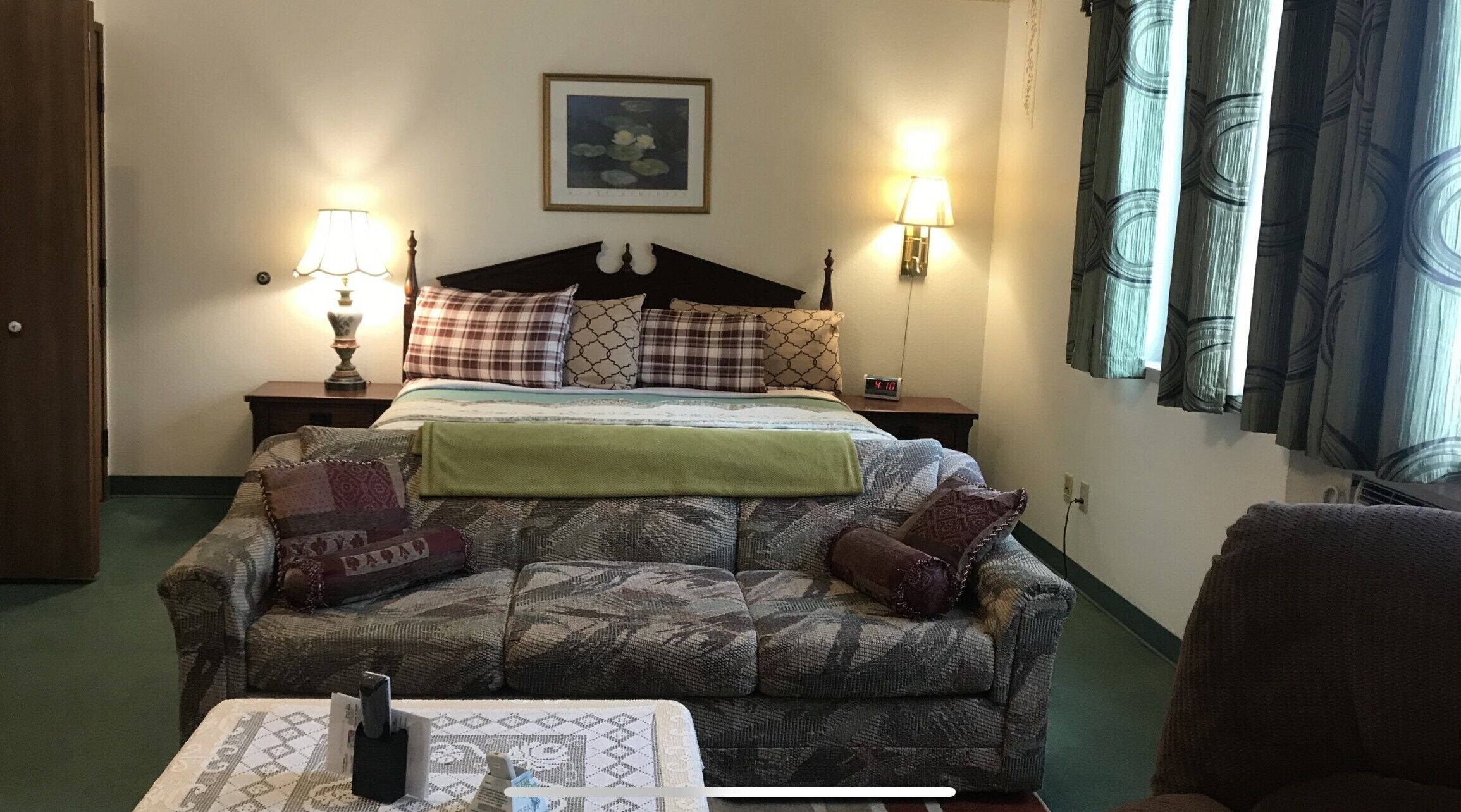 A bedroom with a bed, two bedside tables with lamps, a couch, a chair, and a framed picture on the wall.