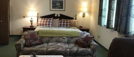 A bedroom with a bed, two bedside tables with lamps, a couch, a chair, and a framed picture on the wall.