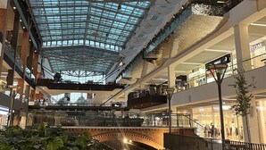 A multi-level shopping mall with a glass ceiling, a central water feature, and multiple retail stores. - Kauris Apartament (Gdańsk)