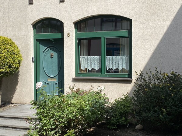 A building with a green door and two windows with lace curtains.