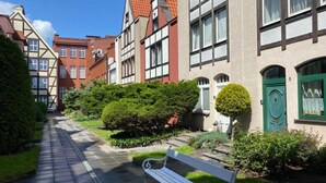 A narrow cobblestone path leading to a bench in a courtyard surrounded by traditional European-style buildings with visible windows and doors. - Kauris Apartament (Gdańsk)