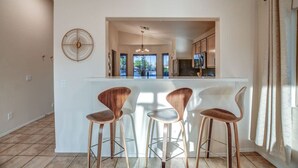 A modern kitchen with a central island, three bar stools, and a large window providing natural light. - Mid Century Themed Home on the Golf Course (San Tan Valley)