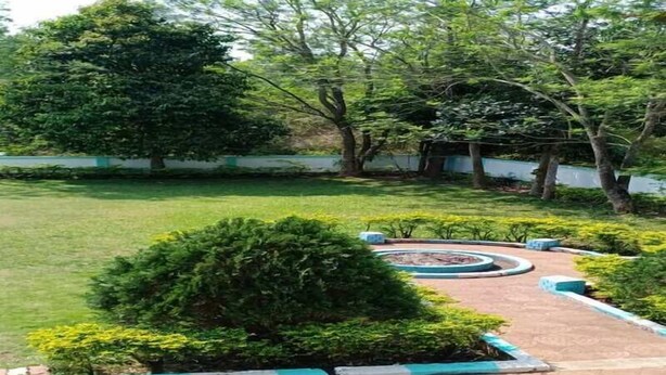 A landscaped garden with a circular flower bed, trimmed hedges, and a paved walkway. - Chandrika Guest House  (Paderu)