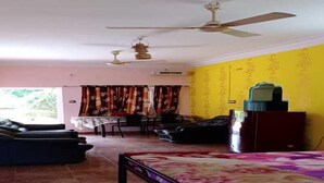 A room with a bed, a ceiling fan, a table with chairs, and a window with curtains. - Chandrika Guest House  (Paderu)