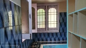 A kitchen with blue and white tiles, a gas stove, and a window with decorative glass panes. - Chandrika Guest House  (Paderu)