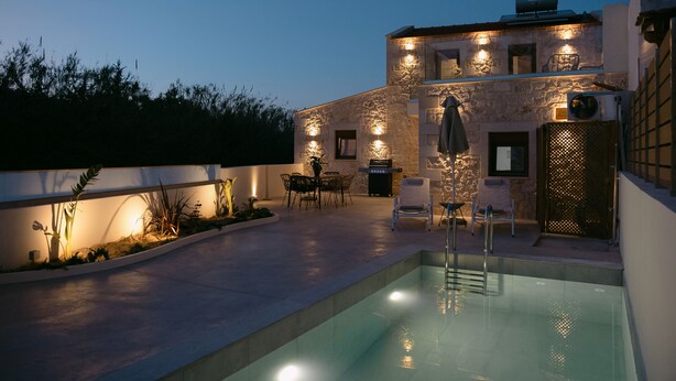 A pool area with a stone building, outdoor furniture, and a well-lit patio. - Fillio luxury villa (Αδελιανός Κάμπος)