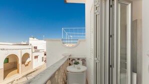 A balcony with a white table and chair, a small potted plant, and a view of neighboring buildings. - 3795 Joy R - Appartamento 3 by Barbarhouse (Manduria)