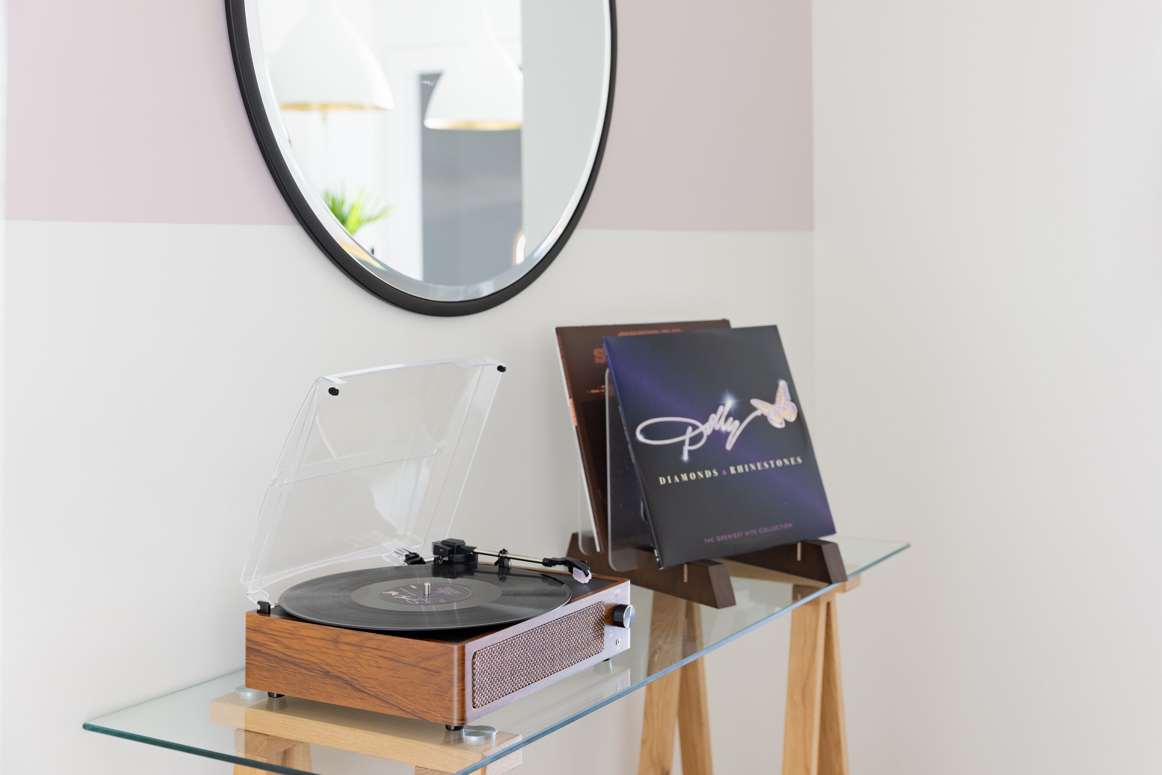 A turntable on a glass table with a book titled "Polly Diamonds & Rhinestones" on an easel.