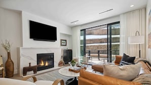 Una sala de estar moderna con chimenea, sofá de cuero y un ventanal con vistas a un paisaje nevado.