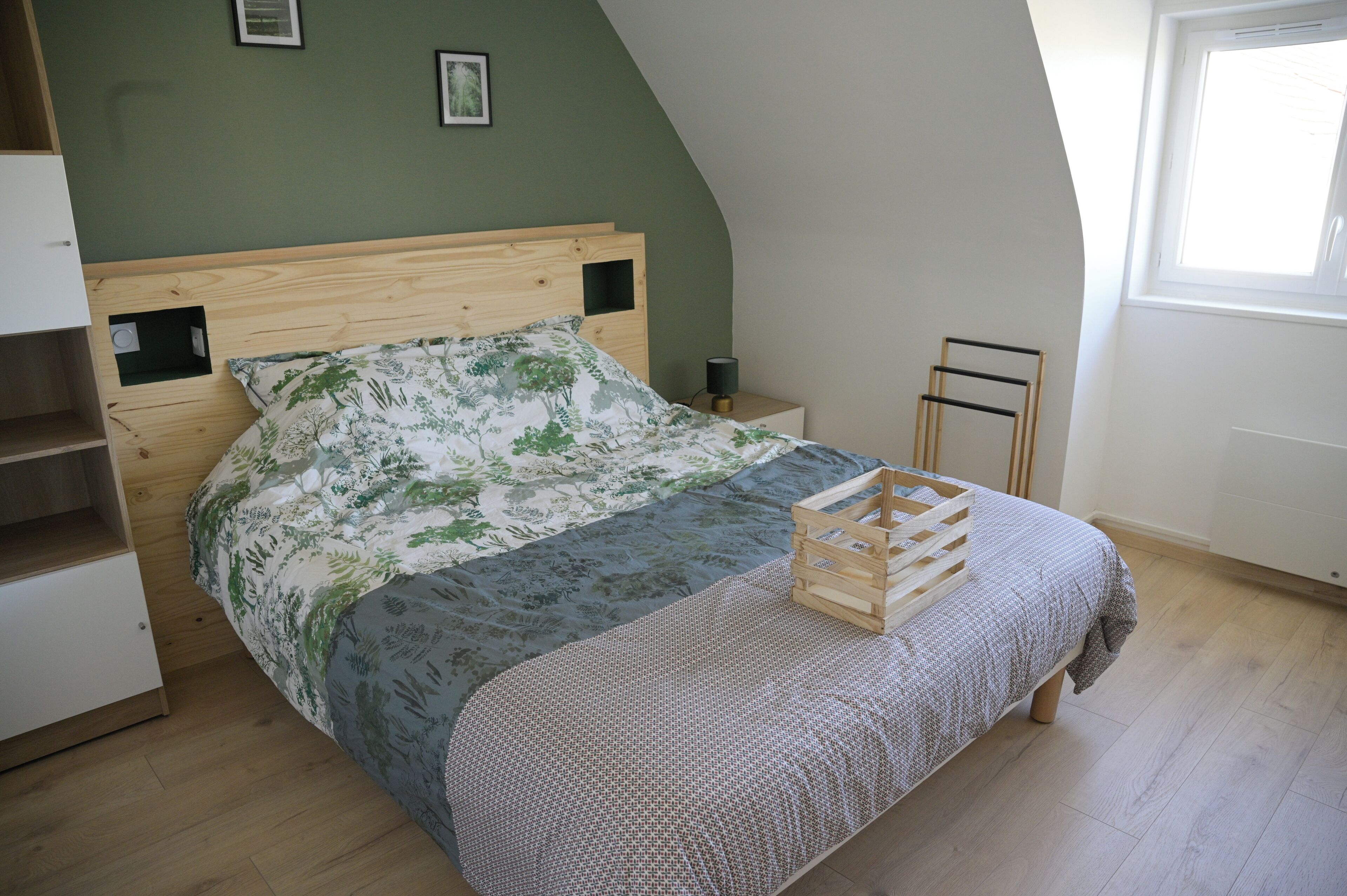 A bedroom with a wooden bed, a nightstand, a small shelf, and a window.