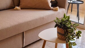A living room with a beige sofa, a small round table with a plant, and a balcony with a white railing. - Casa de Luz - Beach & Boulevard (Torrevieja)
