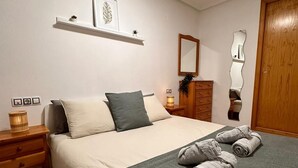 A neatly arranged bedroom with a bed, bedside tables, a mirror, and a wooden wardrobe. - Casa de Luz - Beach & Boulevard (Torrevieja)