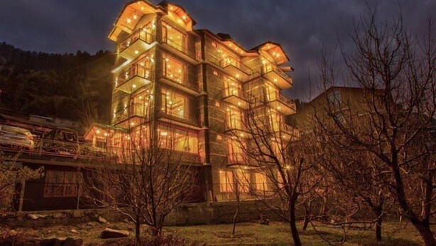 A multi-story building with balconies, surrounded by trees and a hilly landscape. - Sparklyn View (Manali)
