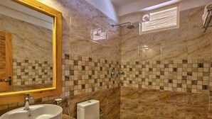 A bathroom with a marble wall, a sink, a toilet, and a shower area. - Sparklyn View (Manali)