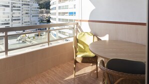 A balcony with a wicker chair and a table, overlooking a cityscape with buildings and a hill. - PRADO, A-5º-52 PK INT 85 (Cullera)