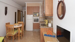 A compact kitchen with wooden cabinets, a microwave, and a sink. There is a dining area with chairs and a table. - PRADO, A-5º-52 PK INT 85 (Cullera)