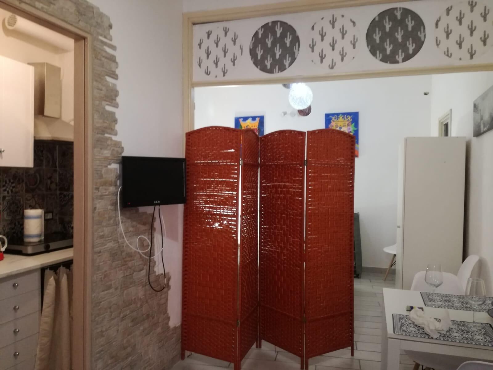 A room with a stone wall, a television mounted on the wall, a red partition, a dining table with a white chair, and a white cabinet.