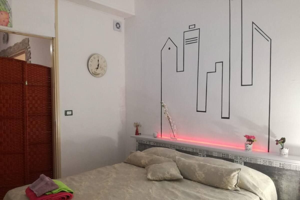 A bedroom with a bed, pillows, a nightstand, a wall clock, and a decorative wall piece.