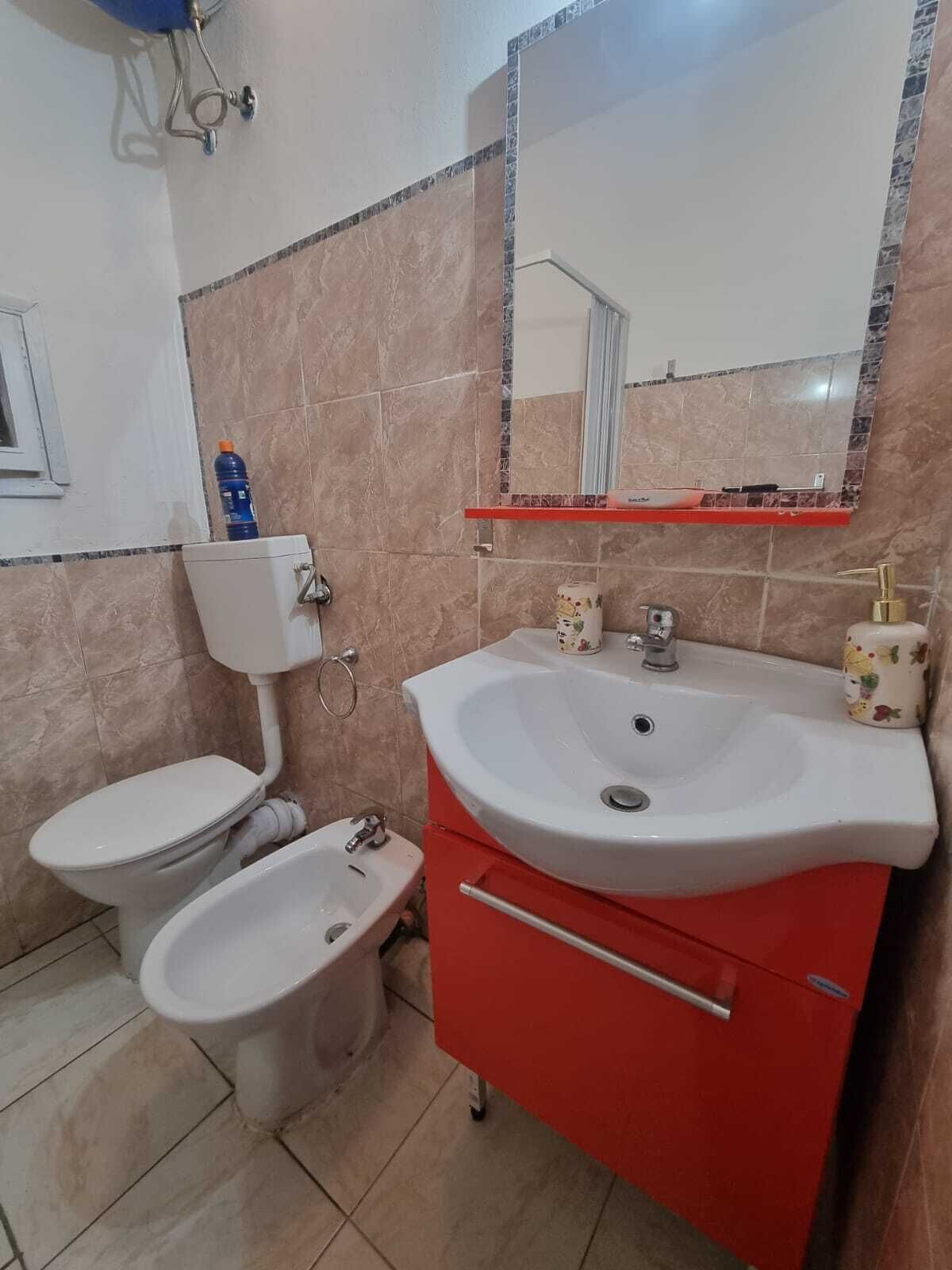 Un bagno con il water, un bidet e un lavandino con un armadietto rosso.