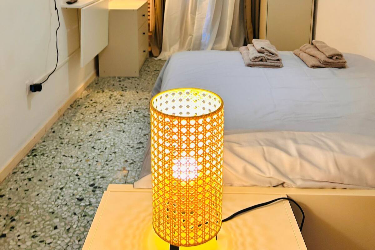 A hotel room with a bed, a desk with a lamp, a TV, and a wardrobe.