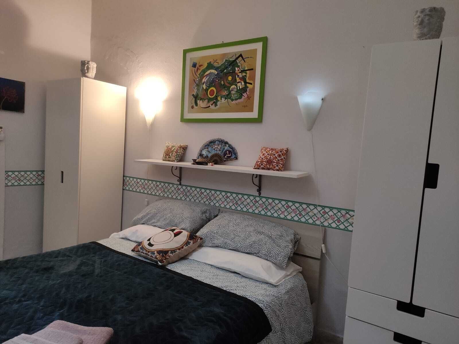 A bedroom with a bed, a wall-mounted shelf with decorative items, a painting, and a wardrobe.