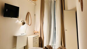 Ein Schlafzimmer mit einem Bett, einem Fernseher, einem Schreibtisch, einem Spiegel und einer Tür.
