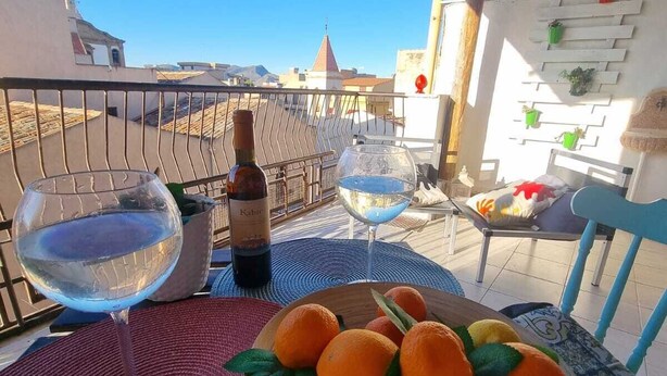 Ein Balkon mit Tisch für zwei Personen, mit einer Weinflasche, zwei Gläsern und einer Orangenschale.