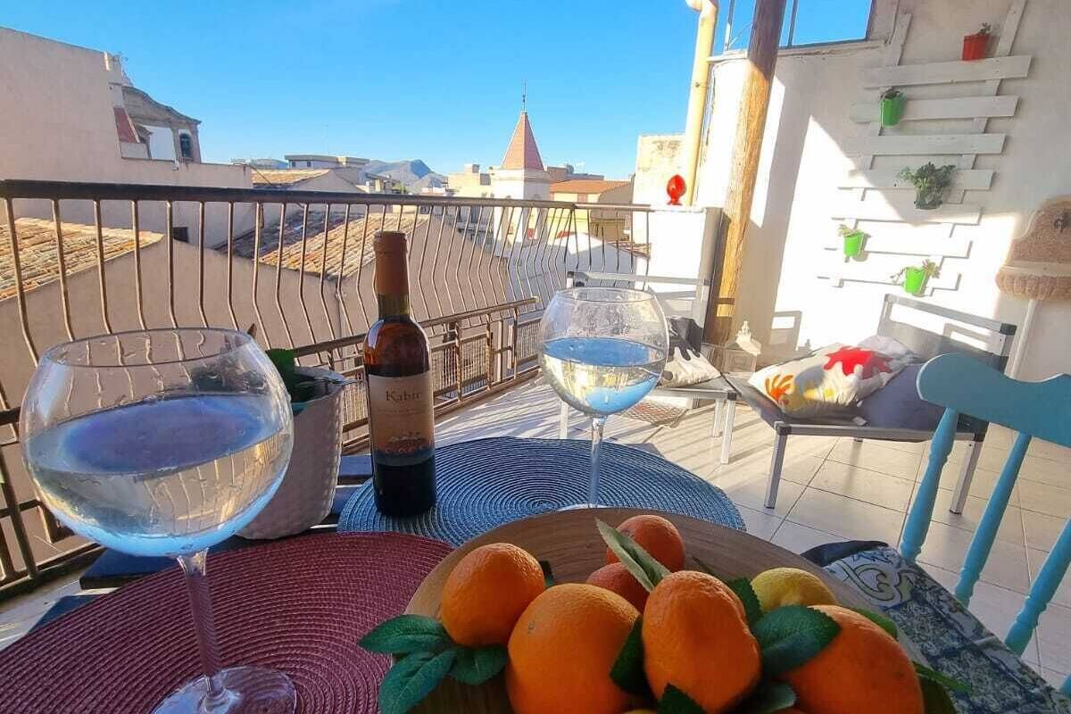 A balcony with a table set for two, featuring a bottle of wine, two glasses, and a bowl of oranges.