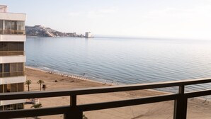 Vista costera desde un balcón con vista a la playa, un edificio con balcón y cielo despejado.