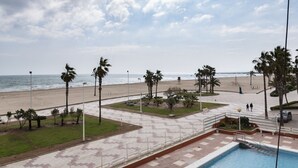 Vista de la playa con zona de piscina, palmeras y cielo despejado.