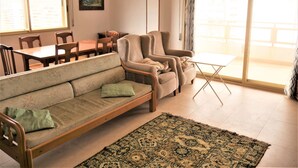 Una sala de estar con sofá, sillas, una mesa de comedor, una mesita auxiliar y un ventanal grande con cortinas.