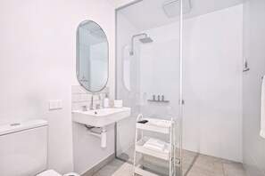 Une salle de bain moderne avec une douche à parois de verre, un lavabo blanc avec un miroir et un meuble de rangement blanc sur roulettes.