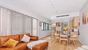 Ein modernes Wohnzimmer mit einem braunen Ledersofa, einem Essbereich mit rundem Tisch und Stühlen, und einer Küche im Hintergrund.