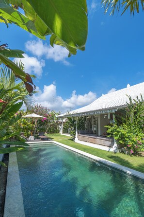 A swimming pool with a white-roofed pavilion, surrounded by lush greenery and a clear blue sky. - Vicolo ArtVillas (Pecatu)