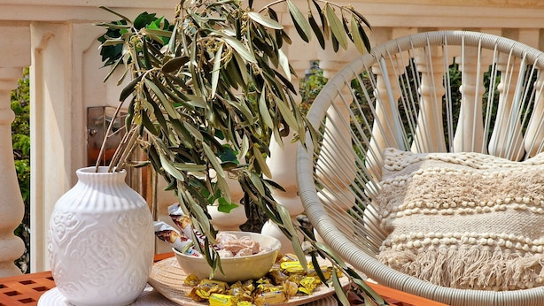 A wicker chair with a cushion, a white vase with a plant, and a plate with wrapped chocolates on a wooden table. - Appartement Ensoleillé Avec Grand Balcon, à 3 Minutes de la mer ! (Rogoznica)