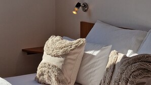 A neatly made bed with fluffy pillows and a blanket, a bedside table with a lamp, and a wall-mounted light fixture. - Appartement Ensoleillé Avec Grand Balcon, à 3 Minutes de la mer ! (Rogoznica)