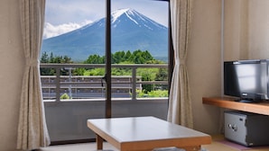 A room with a sliding glass door leading to a balcony, a television, a small safe, and a wooden table with cushions. - SEMINAR PLAZA ROYAL FUJI (Fujikawaguchiko)