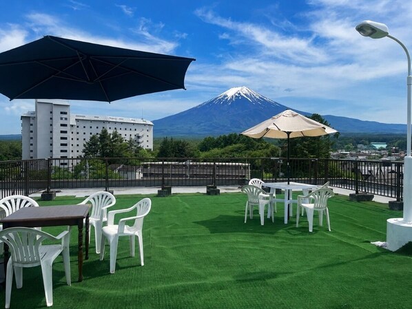 An outdoor seating area with artificial grass, white plastic chairs, and tables, overlooking a mountain.